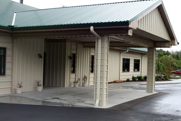 Exterior of a building with light beige siding and a covered entry with green corrugated metal roof.