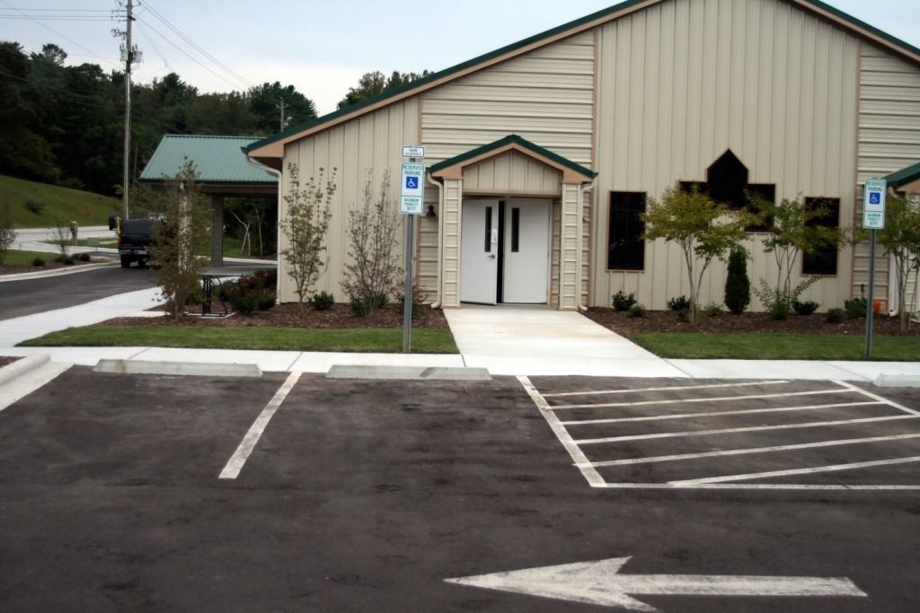Exterior of a light beige building with a white door, accessible parking spaces, and landscaping.