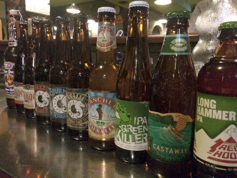 Fila di bottiglie di birra con etichette diverse su un bancone del bar.