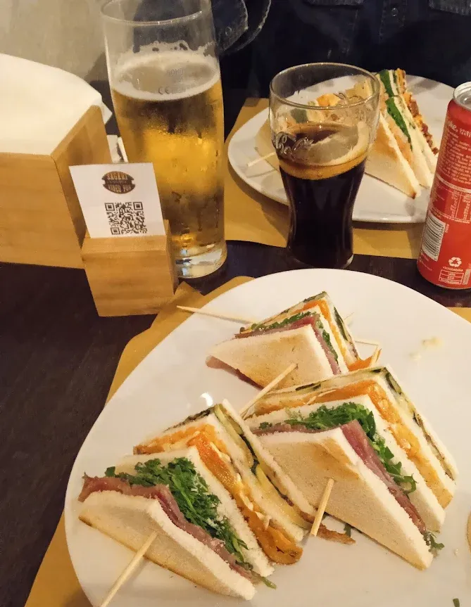 Club sandwich, birra e birra scura su un tavolo con un codice QR.