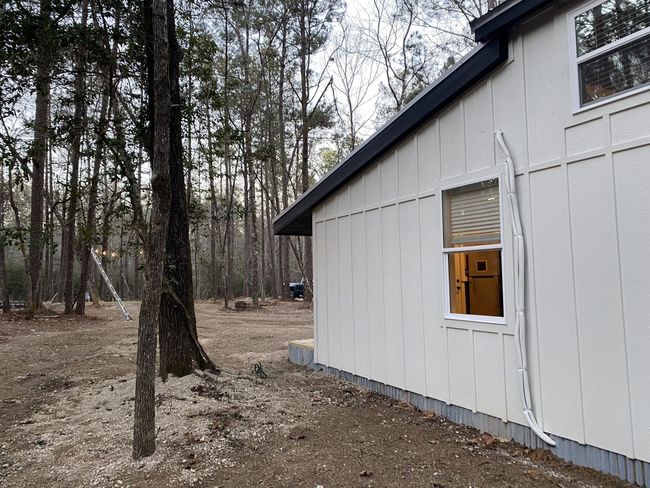 A white house with a window in the backyard is surrounded by trees.