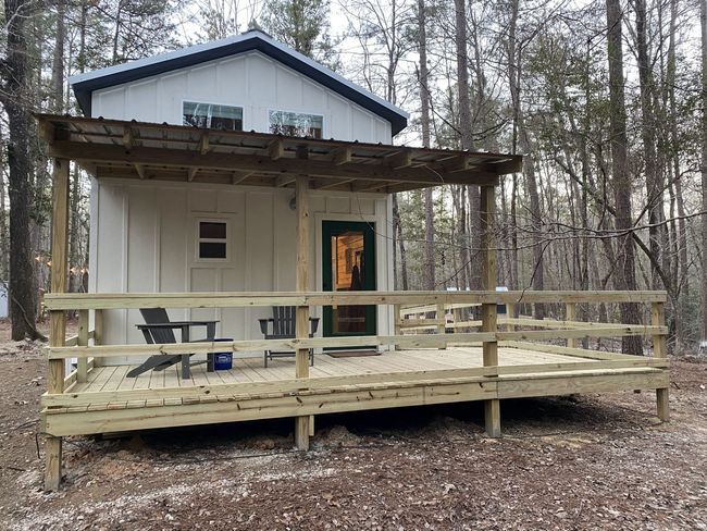 A small white house with a wooden deck in the woods.