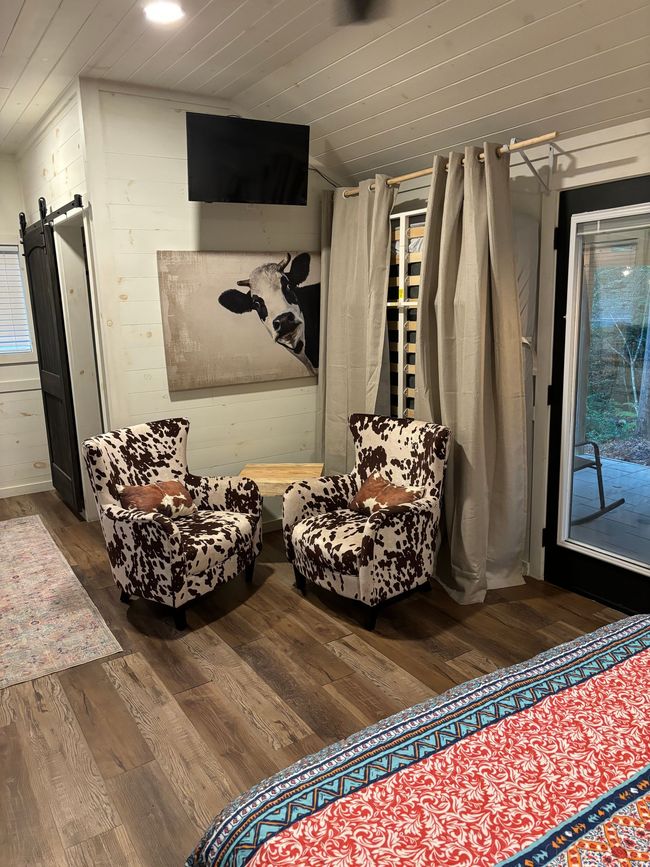 A bedroom with two chairs and a painting of a cow on the wall.