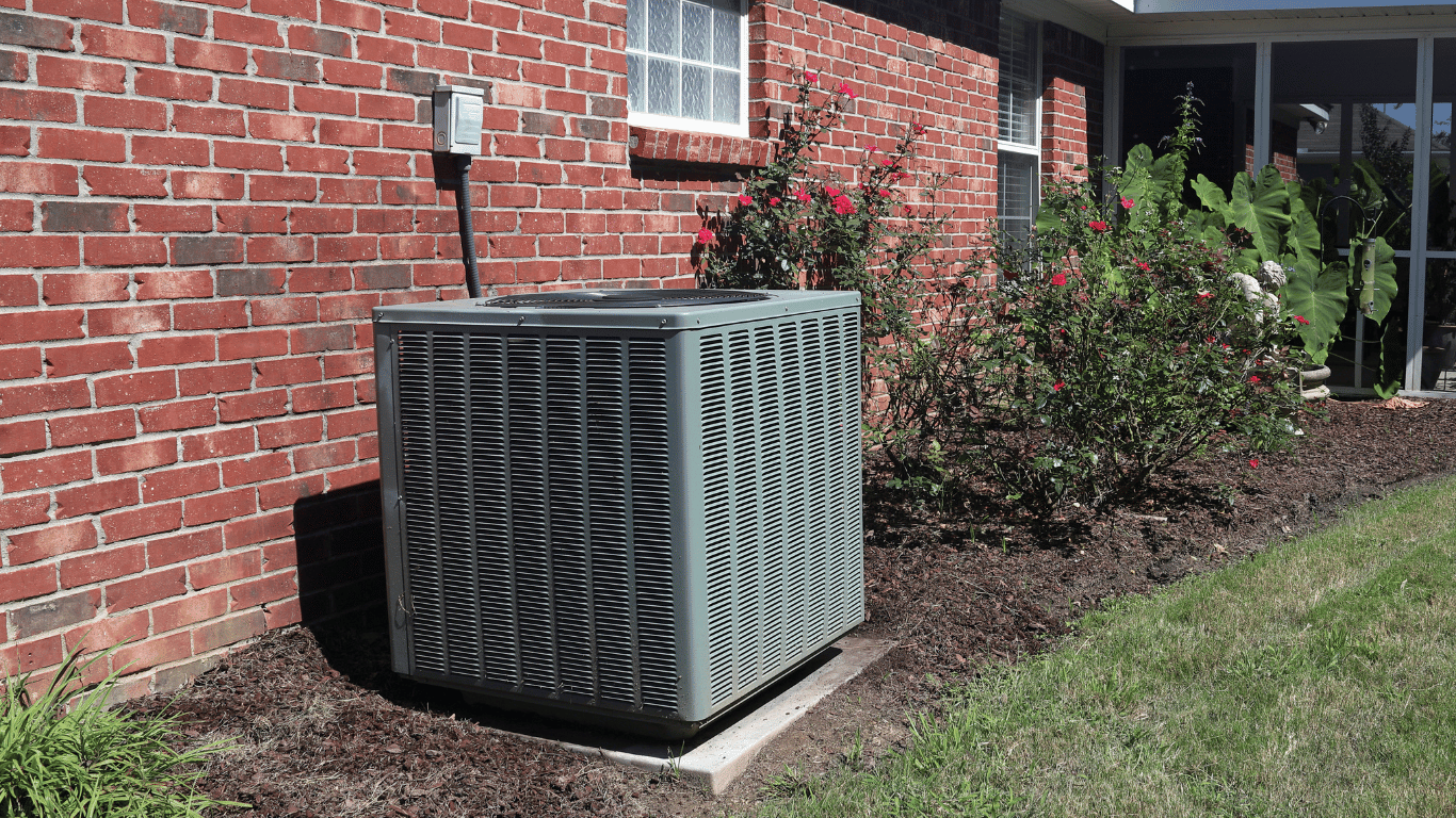 An air conditioner is sitting on the side of a brick house, showcasing a recently completed AC replacement