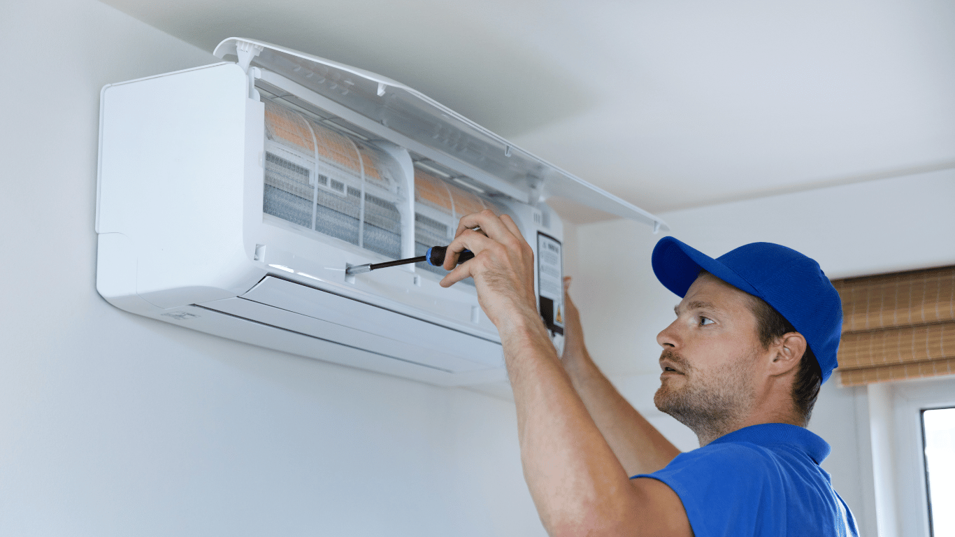 A man is fixing an air conditioner with a screwdriver, performing emergency aircon repairs to restore cooling quickly.