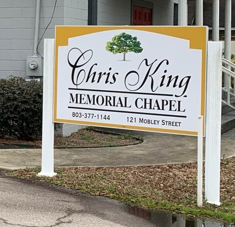 Sign for Chris King Memorial Chapel, white letters on gold and white background, tree graphic.