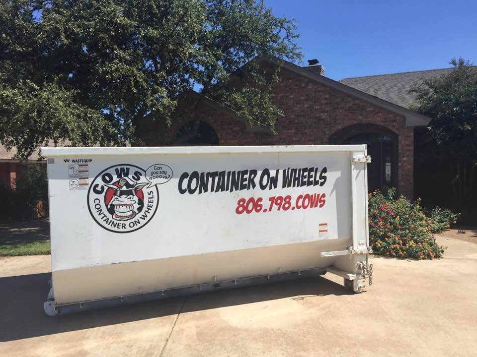 White dumpster with "Container on Wheels" text in front of a brick house.