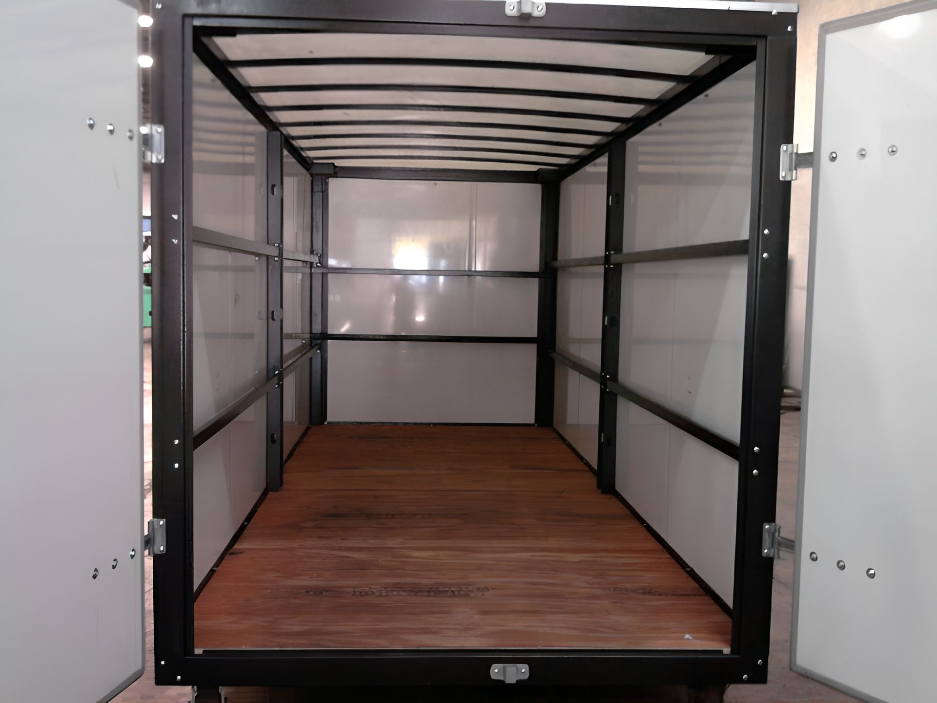 Empty cargo box interior with wooden floor, white walls, and black frame. Doors are open.