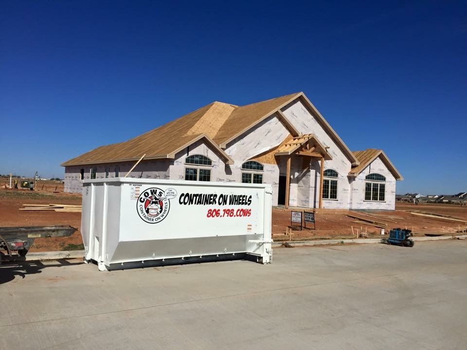 Construction site with a new house and a white dumpster on a sunny day.