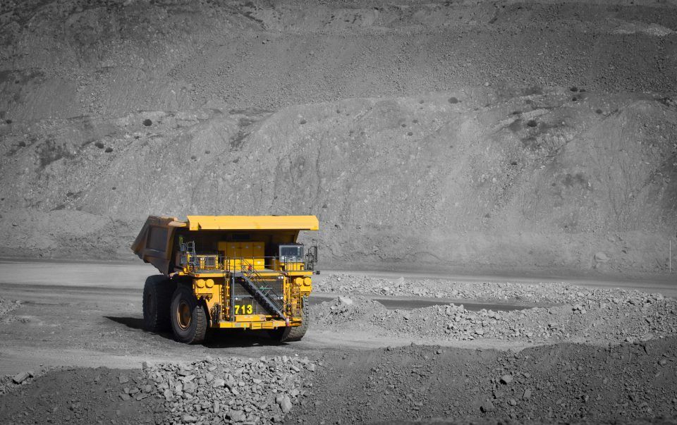 A yellow dump truck is driving down a dirt road.