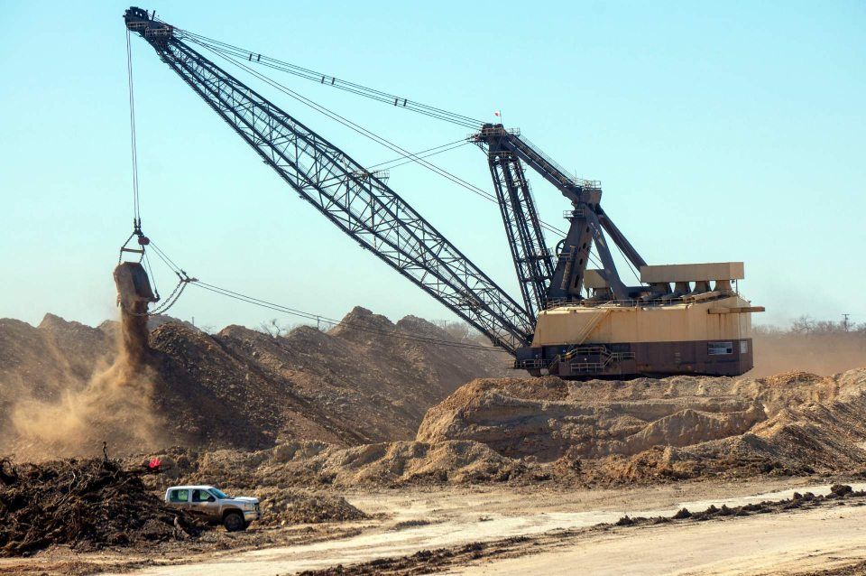 A large crane is loading dirt into a truck.