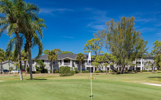 Golf course green with a flag, palm trees, and condos under a clear blue sky at Belvedere at Quail Run in Naples, FL.
