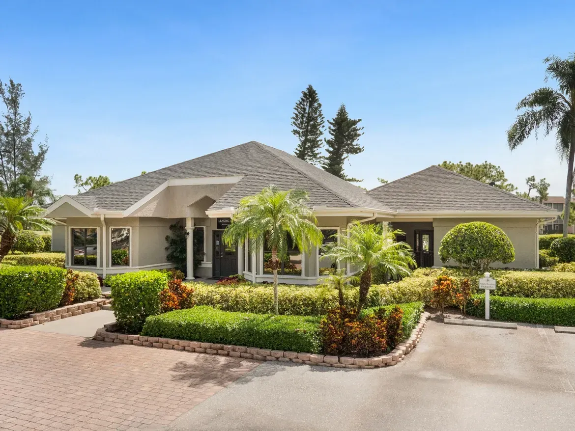 A large house with a driveway and palm trees in front of it at Belvedere at Quail Run in Naples, FL.