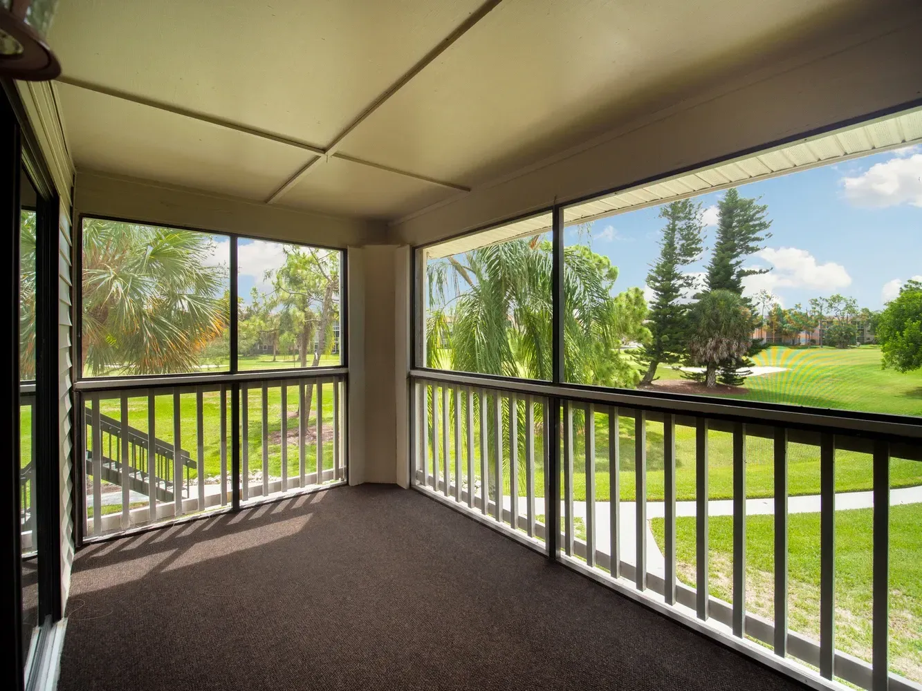 An empty screened in porch with a view of a golf course at Belvedere at Quail Run in Naples, FL.