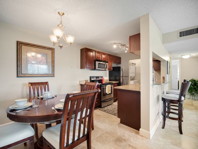 Dining area with round wooden table, chairs, and open kitchen with dark cabinets at Belvedere at Quail Run in Naples, FL.