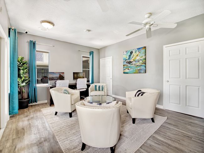 Living room with white chairs, rug, teal curtains, and art on a gray wall.