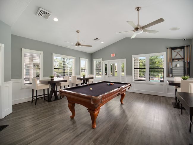 Pool table in a room with tall windows, tables, and ceiling fans.