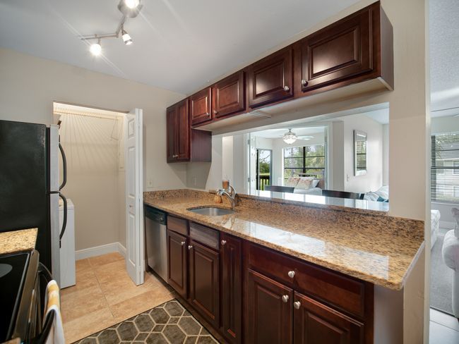 Kitchen with dark cabinets, granite countertop, and pass-through to a living area.