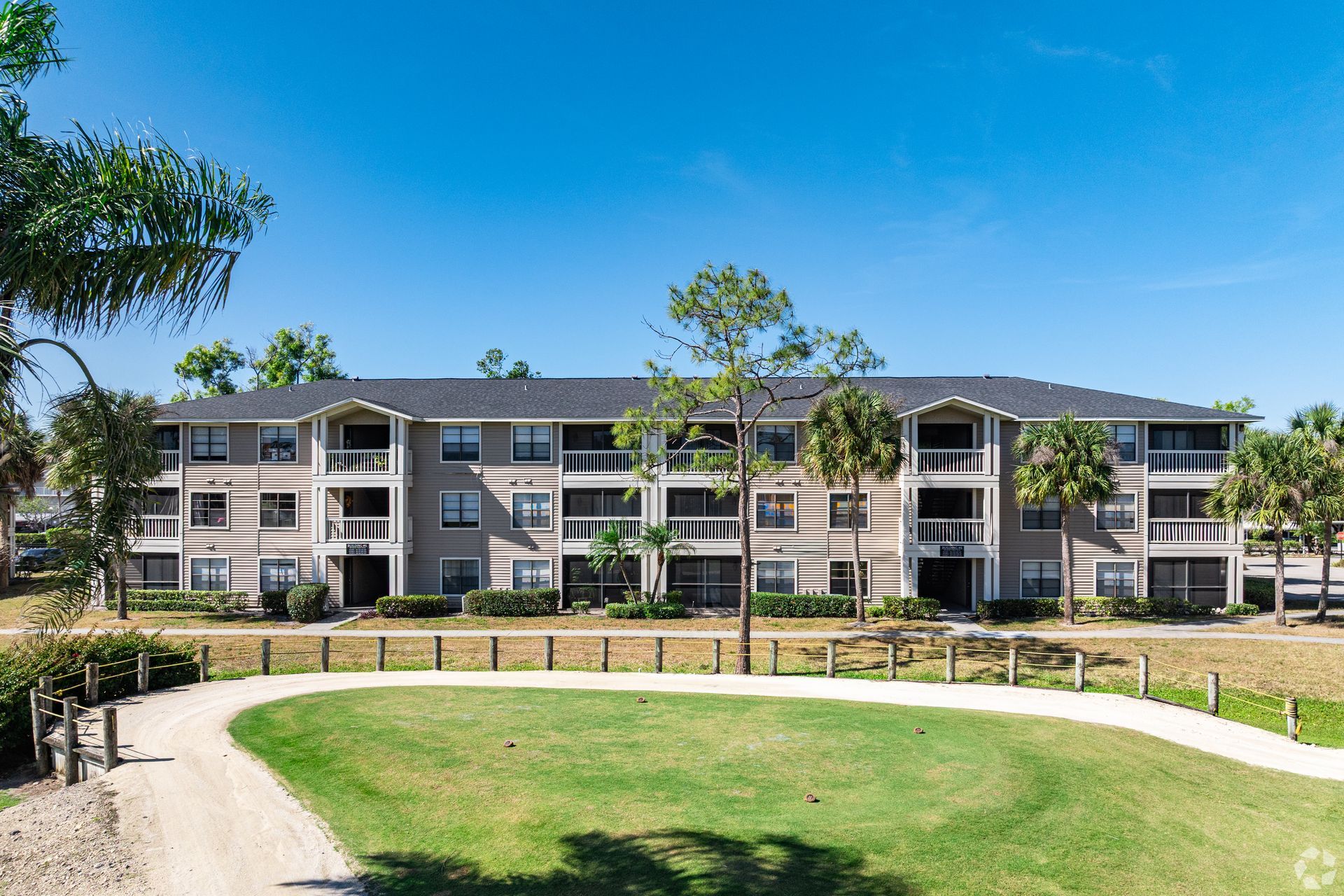 Belvedere at Qual Run apartments with a golf cart path and palm trees beside a green lawn under a bright blue sky