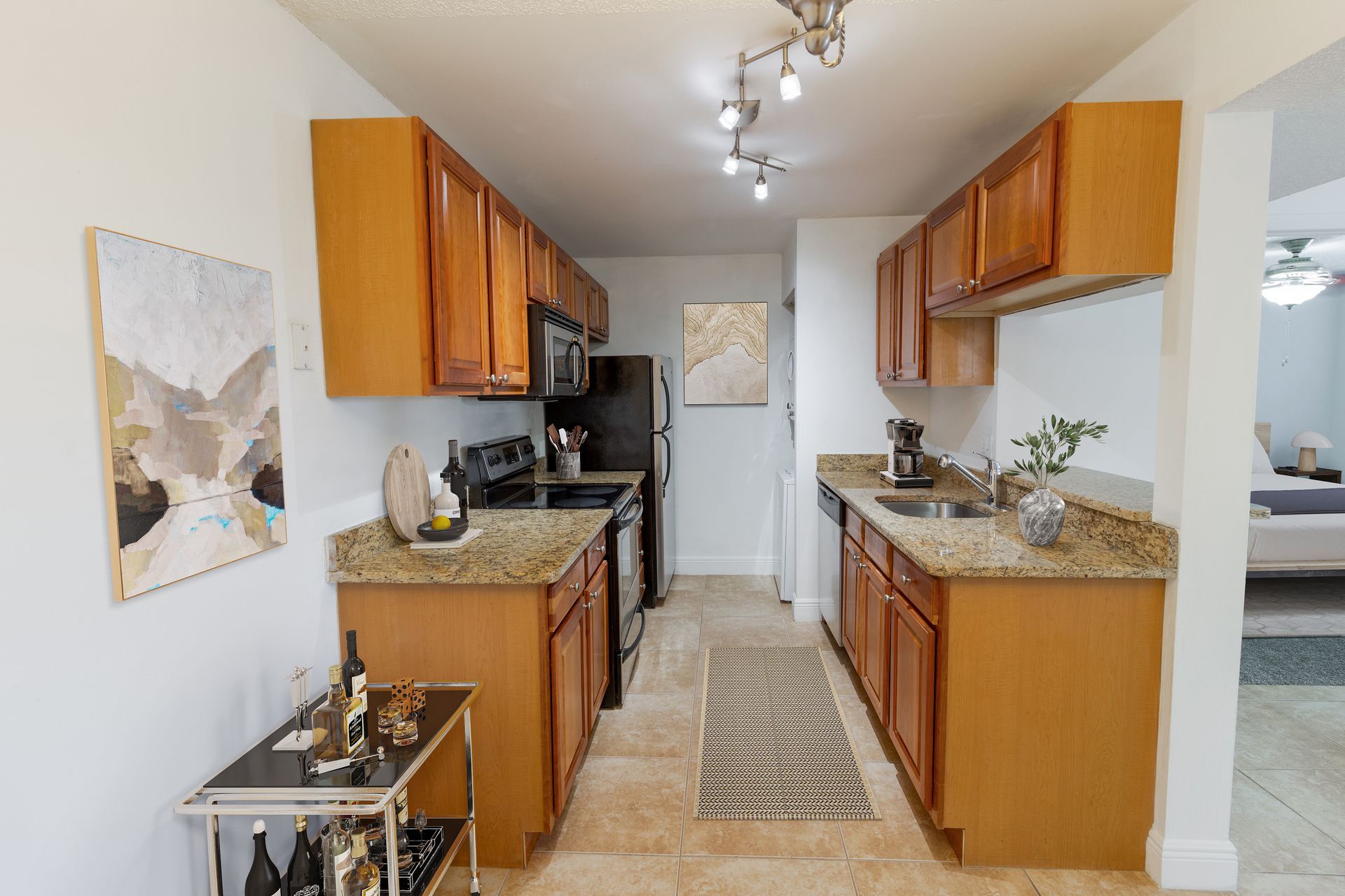A galley kitchen with light wood cabinets, granite countertops, and a wine cart at Belvedere at Quail Run in Naples, FL.