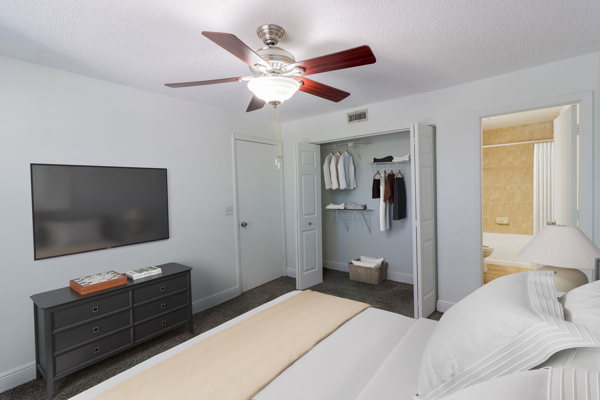 Bedroom with a bed, TV, dresser, open closet, and a doorway to a bathroom at Belvedere at Quail Run in Naples, FL.