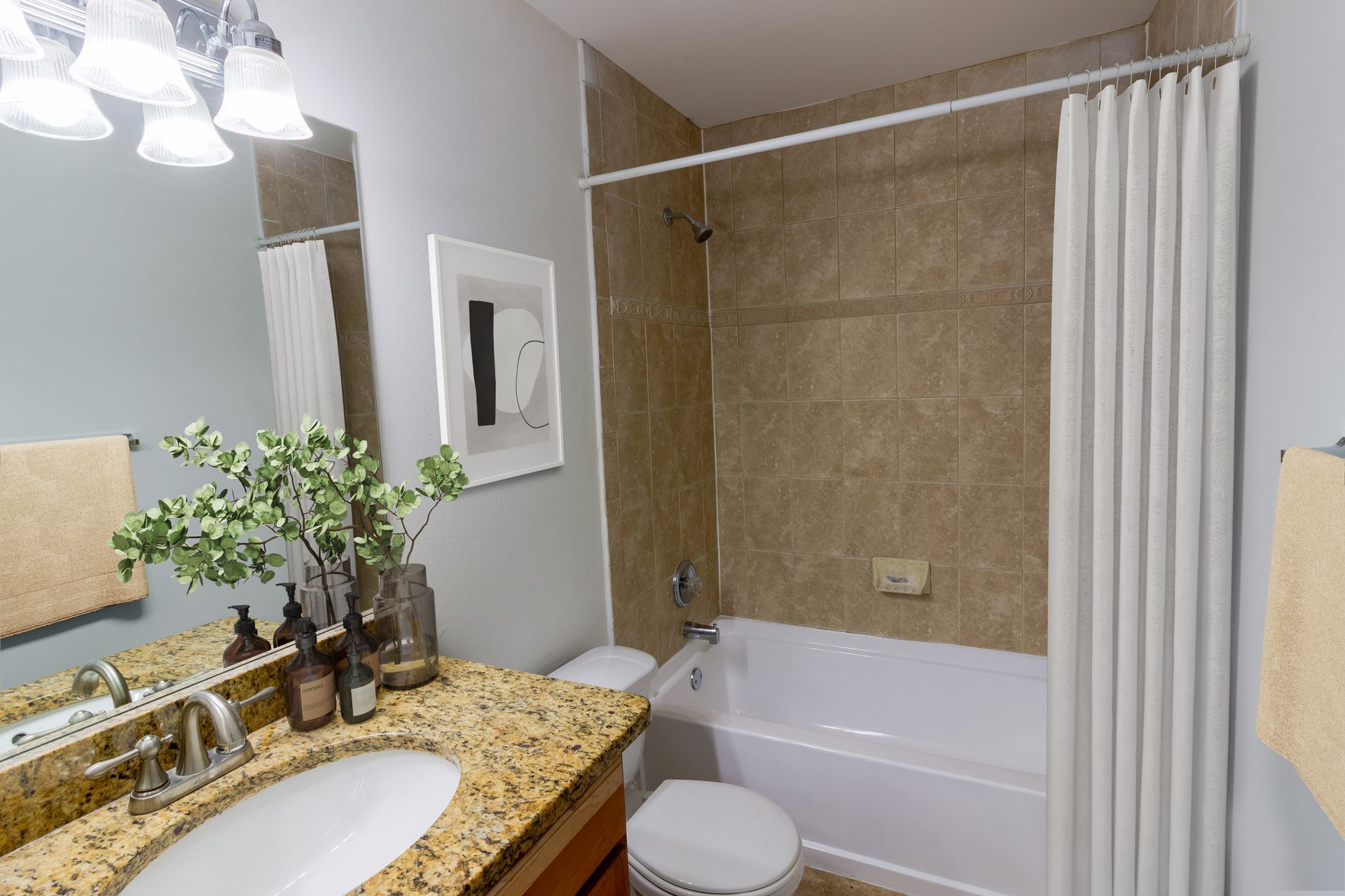 Bathroom with beige tile, white tub, and vanity with a granite countertop at Belvedere at Quail Run in Naples, FL.