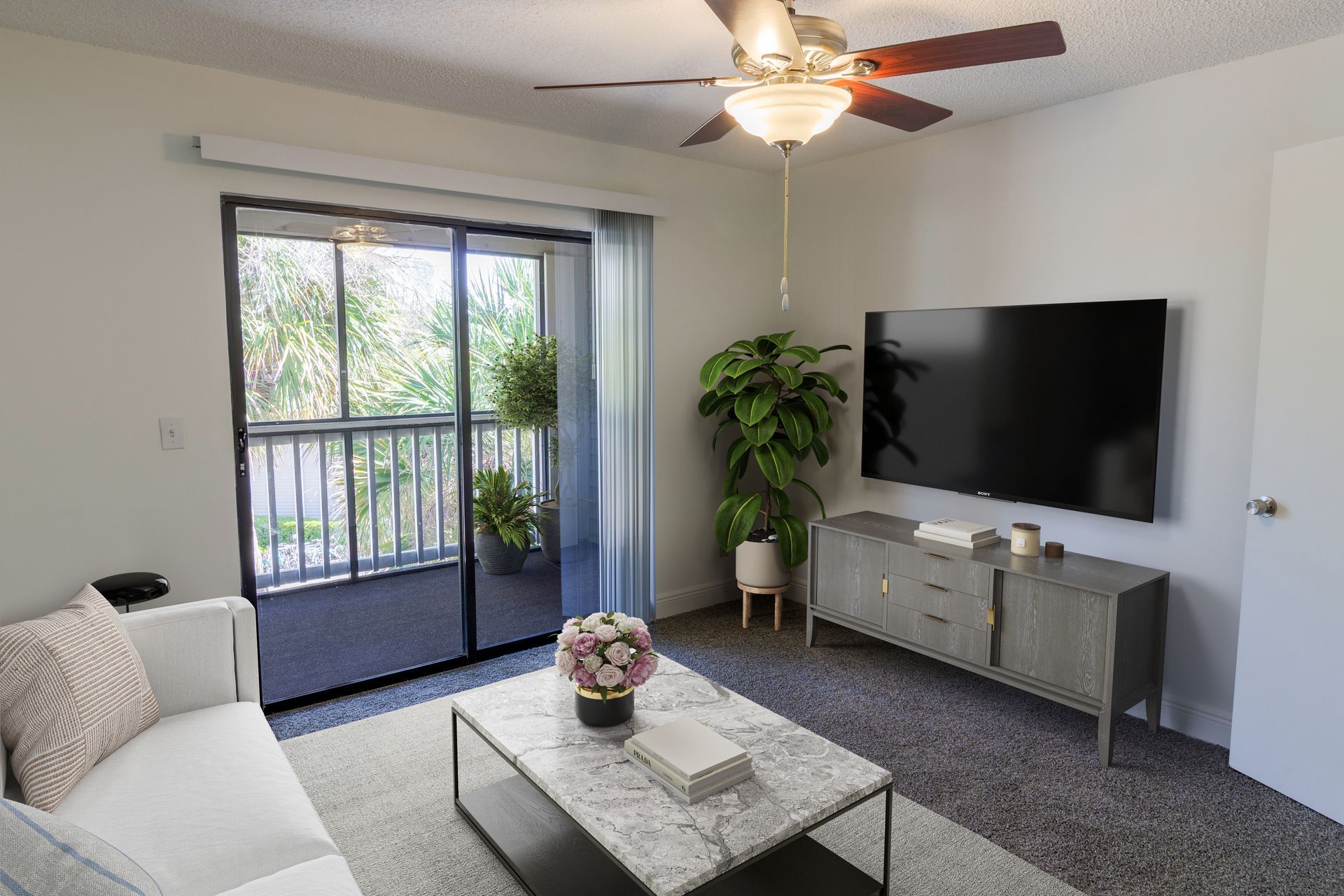 Living room with sliding glass door to balcony, a sofa, TV, and coffee table at Belvedere at Quail Run in Naples, FL.