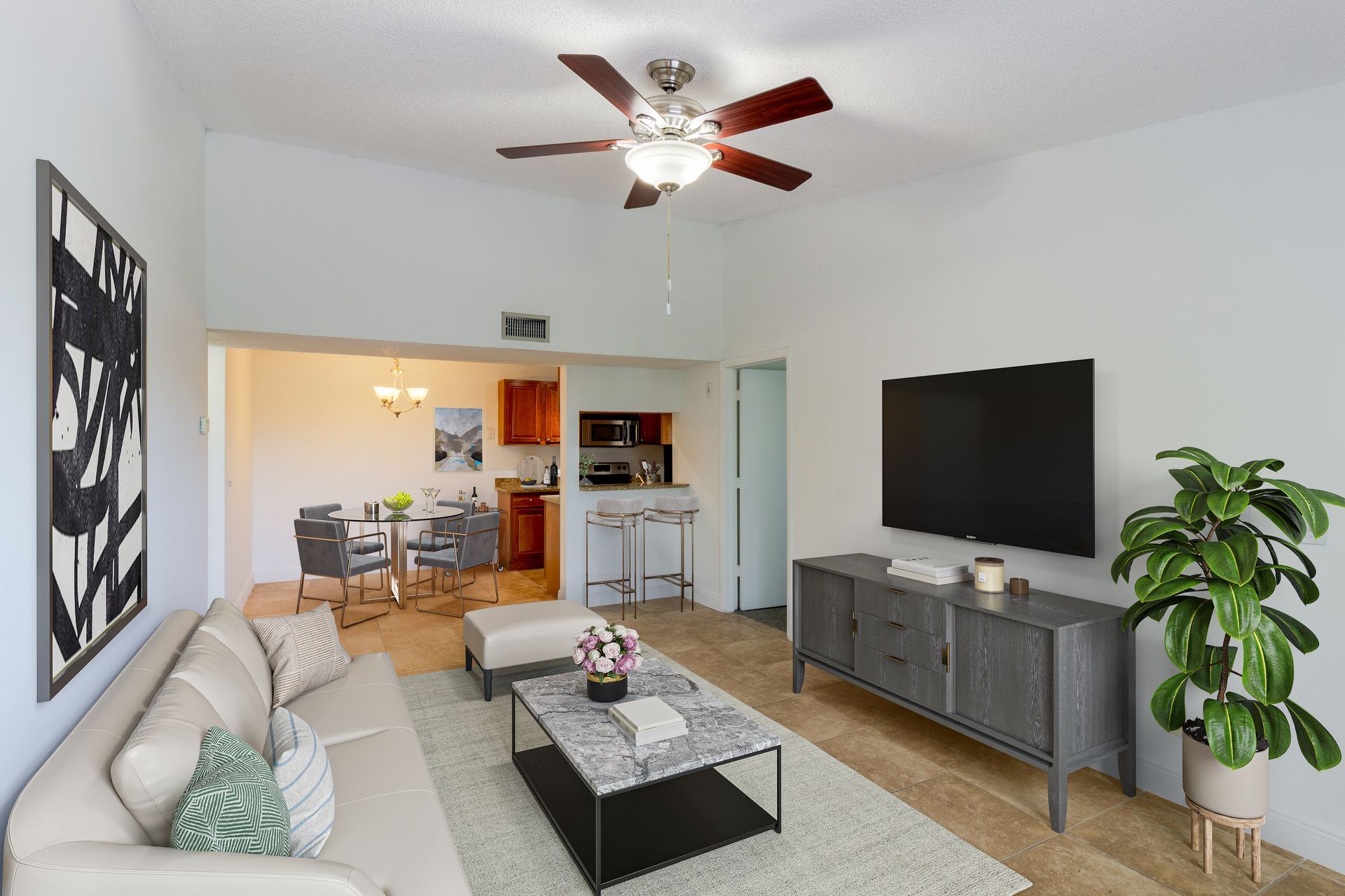 Living room with couch, TV, and dining area. Neutral colors. Plant on the right at Belvedere at Quail Run in Naples, FL..