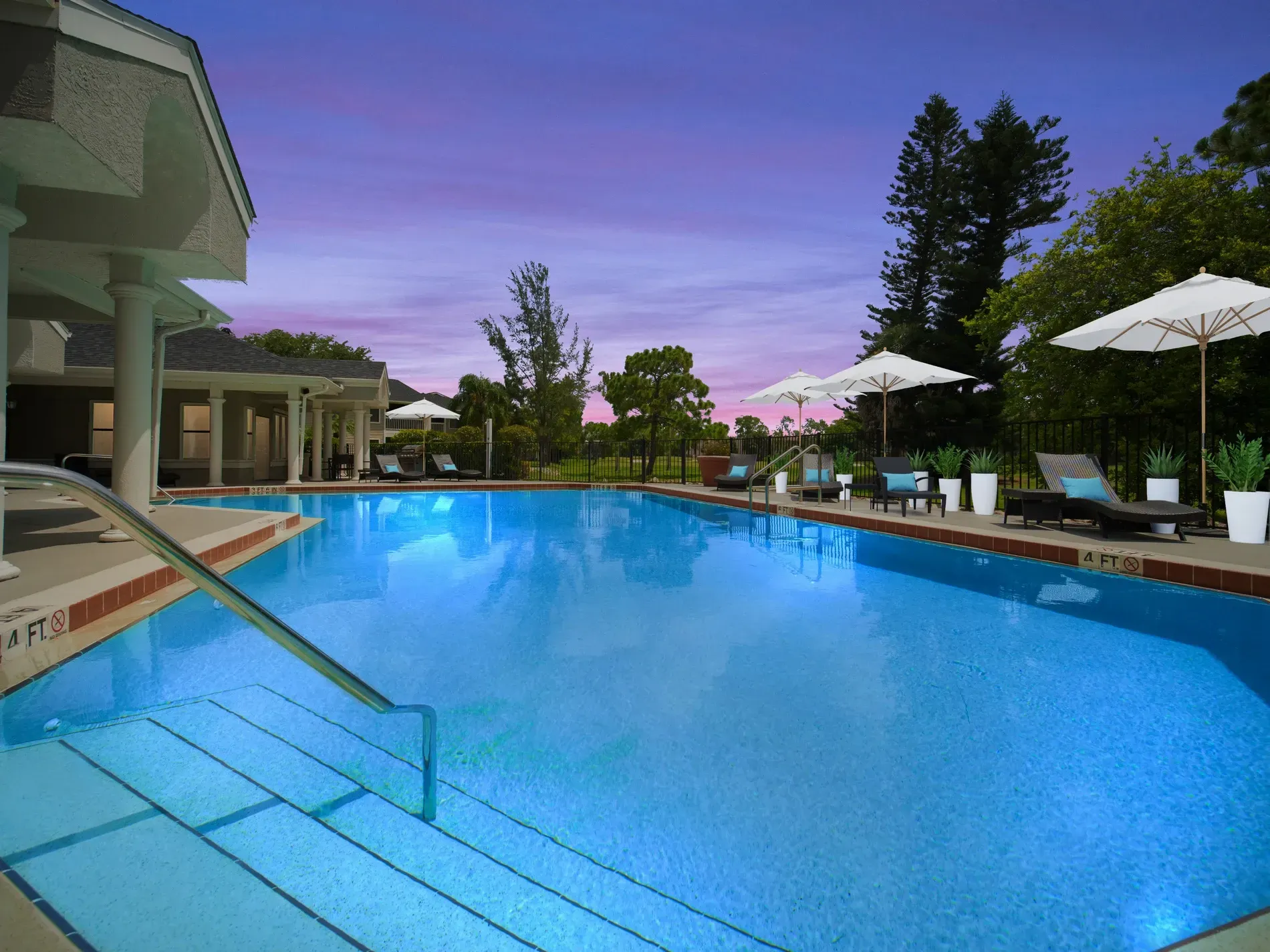 Outdoor swimming pool with lounge chairs and umbrellas, under a dusk sky.