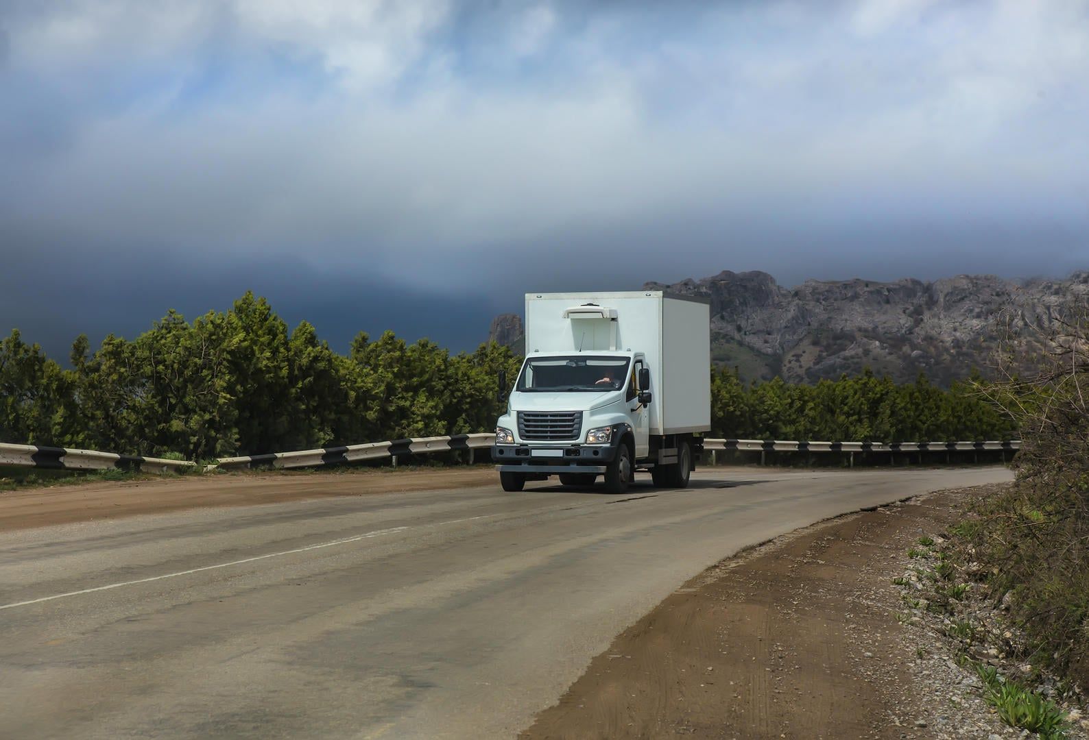 A white truck is driving down a road with mountains in the background.