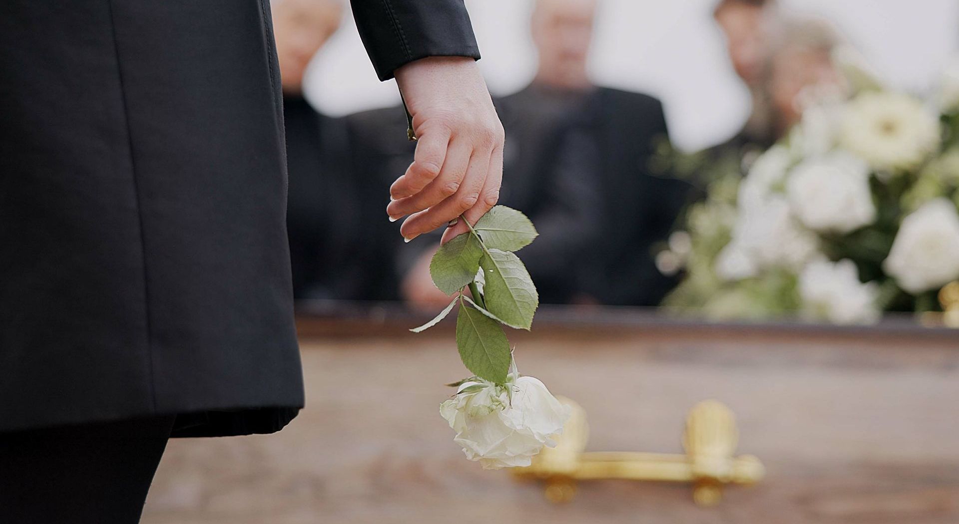 A person is holding a rose in front of a coffin at a funeral.