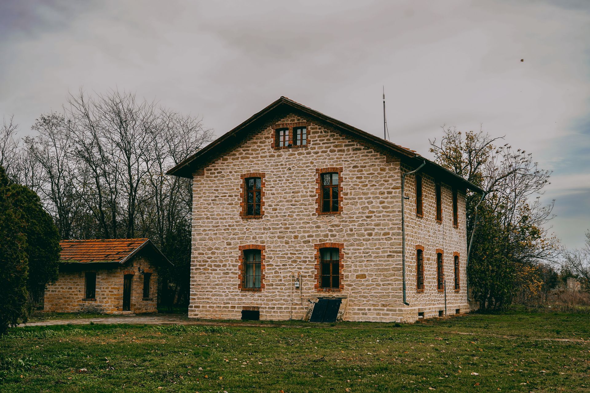 Weathered wooden house with a steep roof and two blue boarded windows, set against greenery.