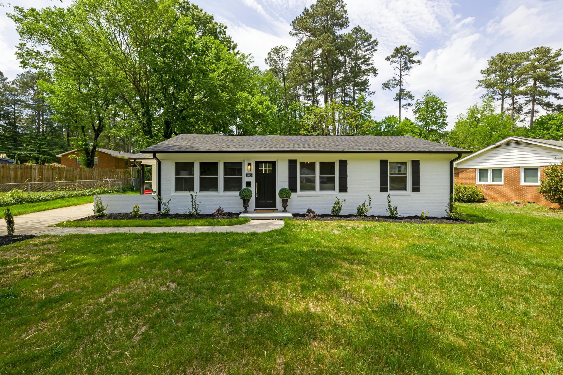 Single-story white house with black shutters, front porch, and a large green lawn under trees
