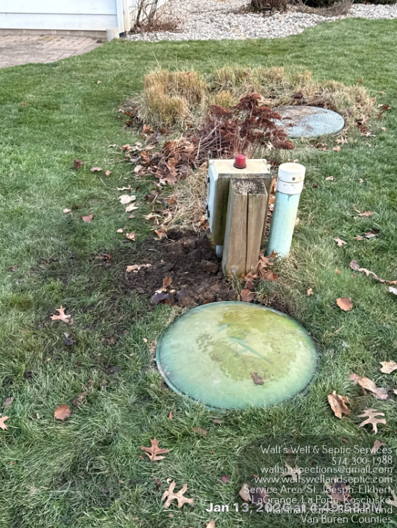 Open manhole with a yellow-and-black cable device and wires inside, surrounded by grass.