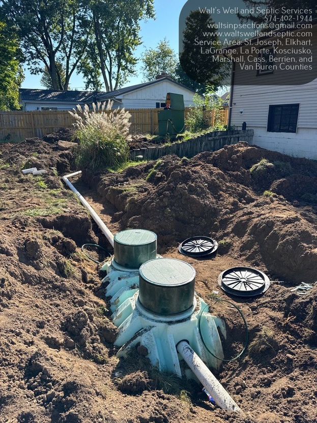 Septic tank lids and pipes exposed in a dirt excavation beside a house and shed in Elkhart, Indiana