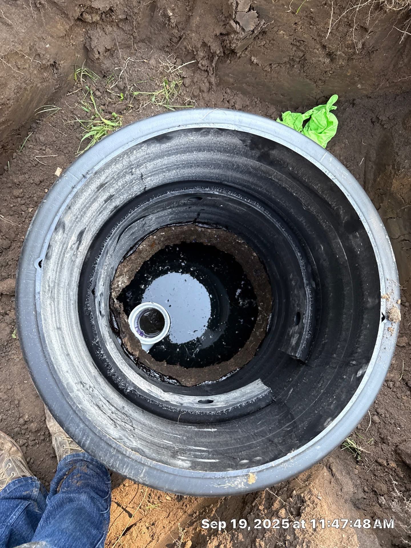 Open manhole with a yellow-and-black cable device and wires inside, surrounded by grass.