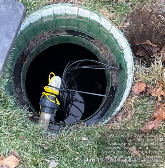 Utility box and white pipe cover in a grassy yard beside a stone ring and bare shrubs