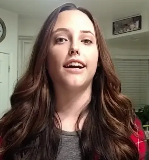 A woman with long brown hair is smiling in a living room.