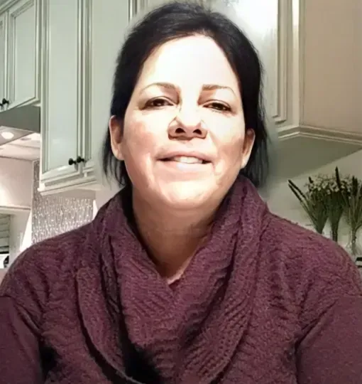 A woman in a purple sweater and scarf is smiling in a kitchen.