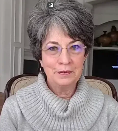 A woman wearing glasses and a sweater is sitting in a chair.