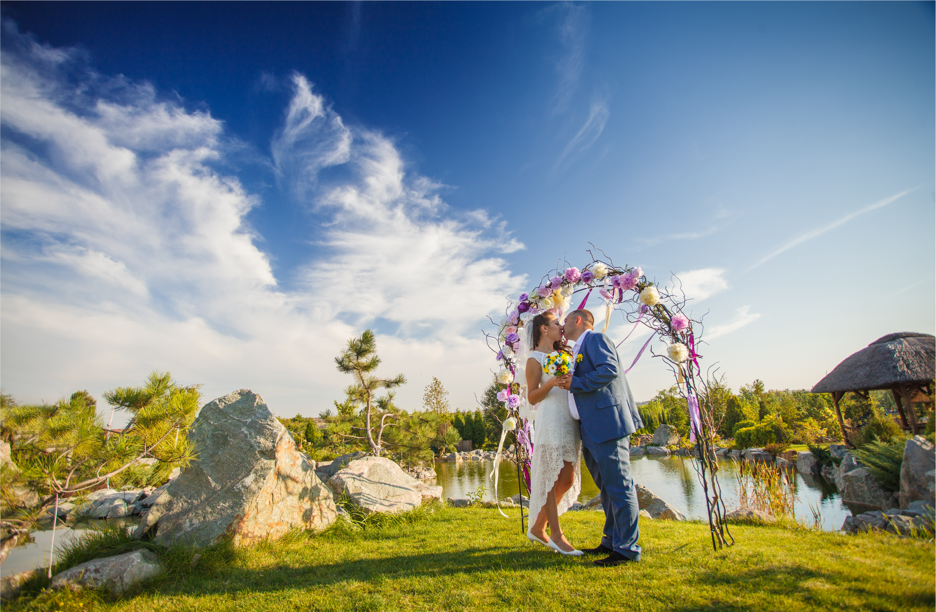 A bride and groom are kissing under a floral arch.