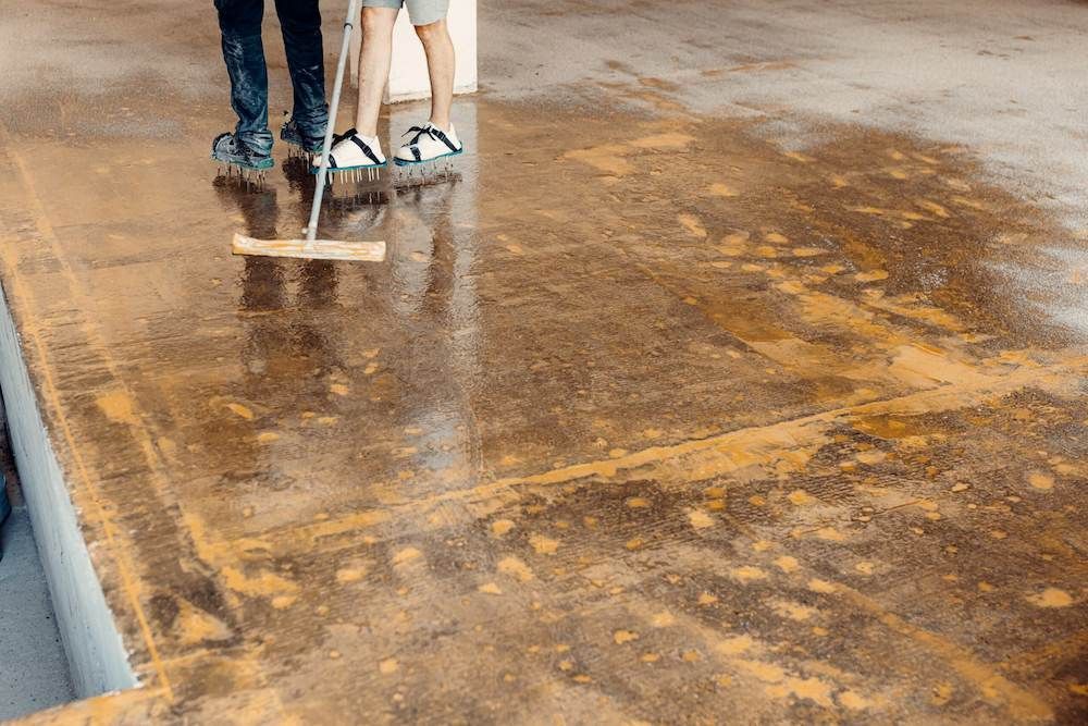 Two People Are Cleaning a Dirty Concrete Floor with A Mop — Slippery Solutions In Cranbrook, QLD 