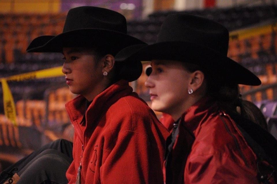 Two people in black cowboy hats and red jackets seated indoors under warm lighting