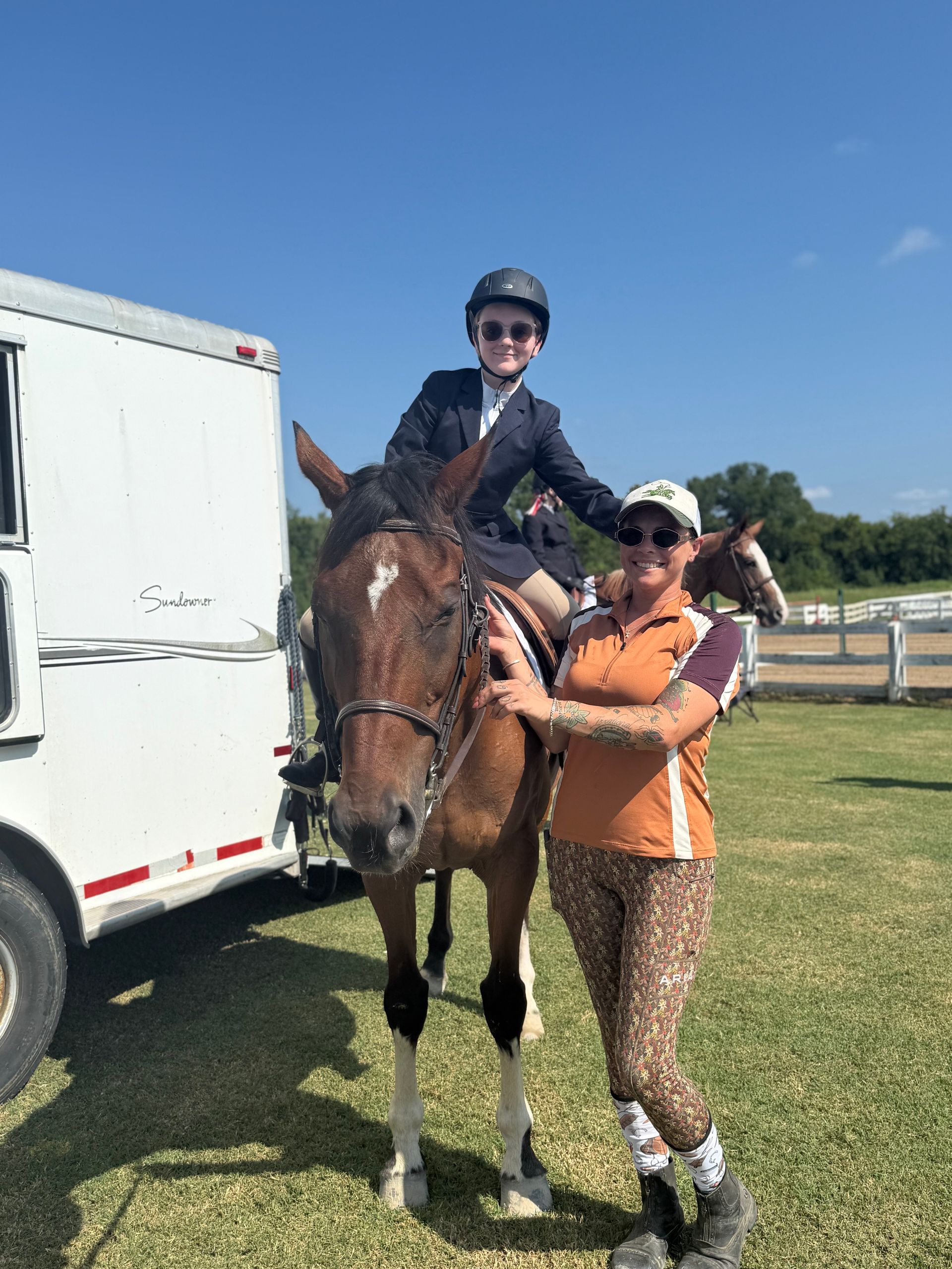 Child on horse with an adult handler beside a horse trailer on a sunny day.