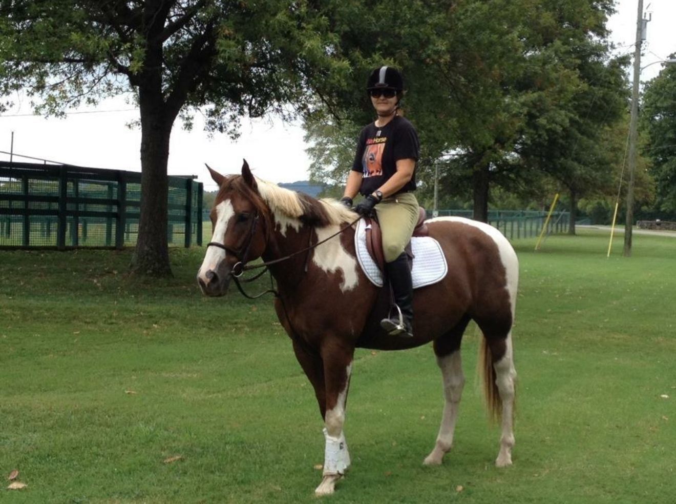 Woman riding a brown and white paint horse in a grassy field.