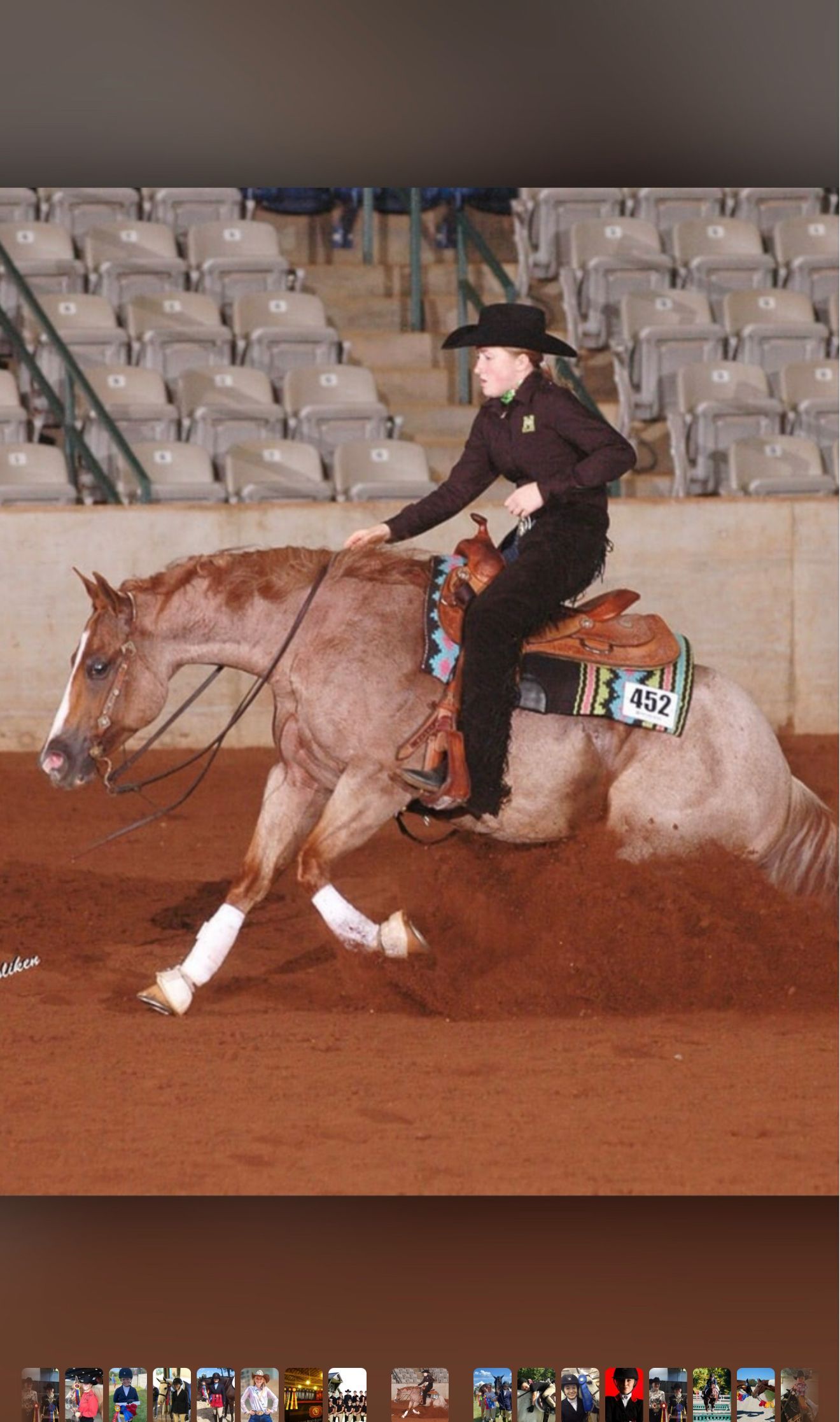 Person riding a horse in an indoor arena, wearing a black hat and shirt, with empty bleachers behind.