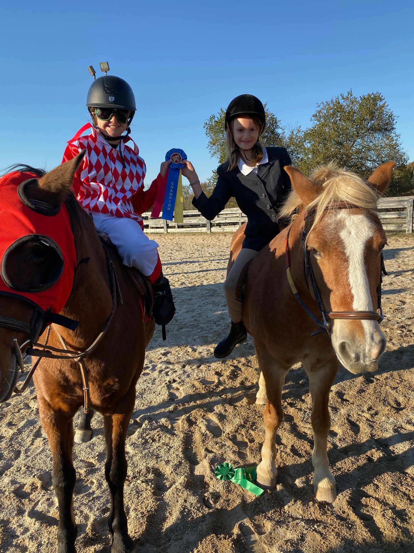 Two riders on horses at an outdoor arena, one in a red-and-white patterned shirt and helmet