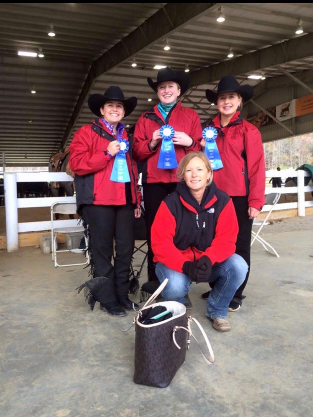 Four people in red shirts and black cowboy hats pose in a barn, holding ribbons and a trophy.