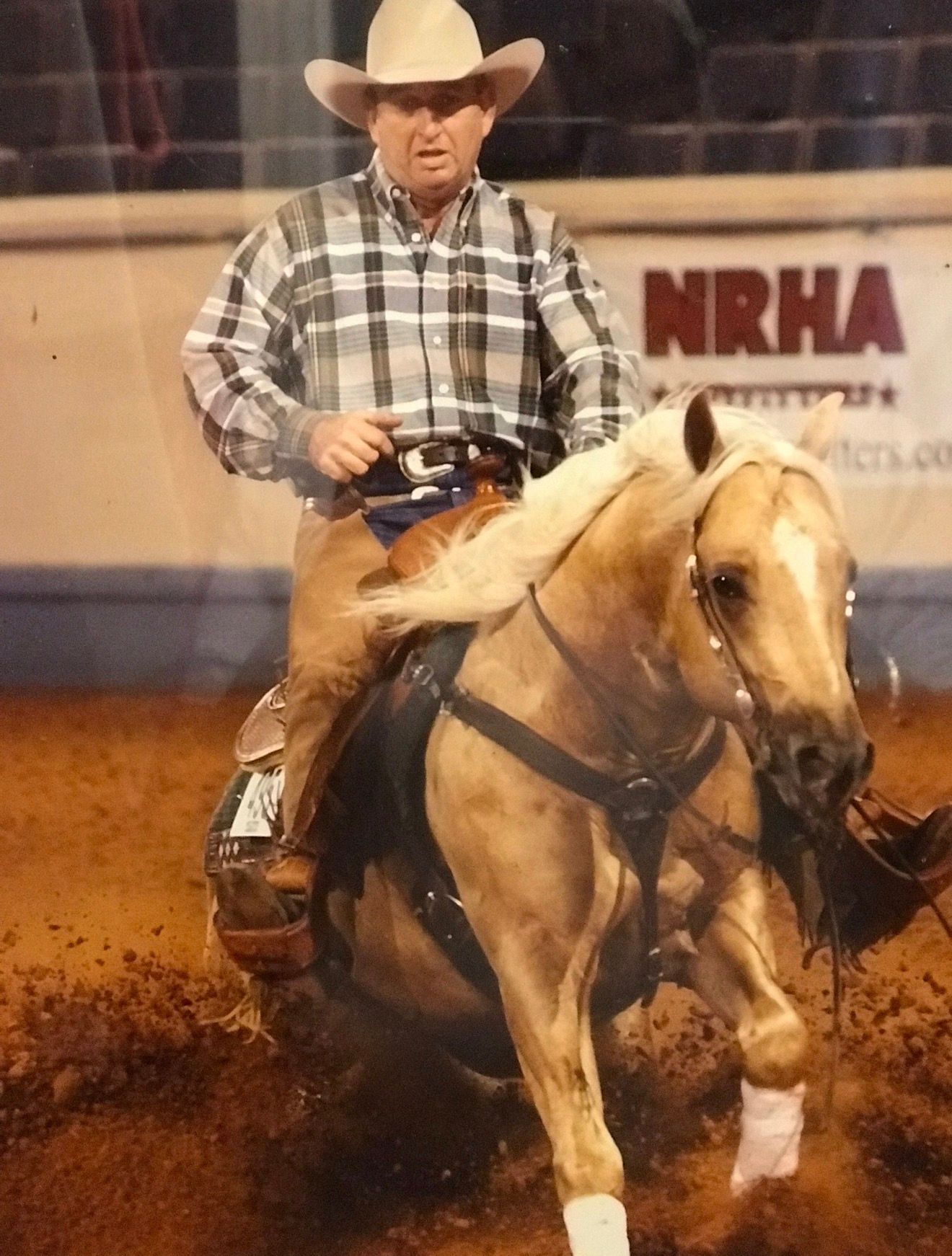 Cowboy in a white hat riding a palomino horse in a rodeo arena, kicking up dirt.