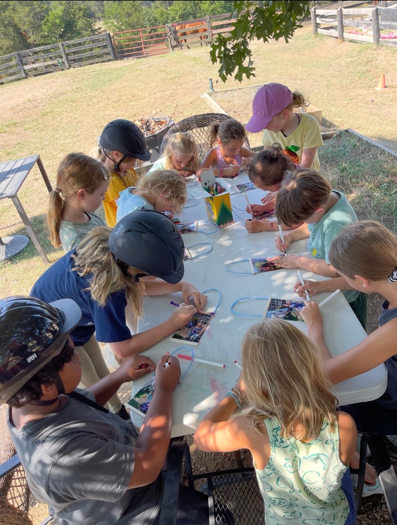 Children gathered around a picnic table outdoors, painting and crafting with brushes and colored paper.